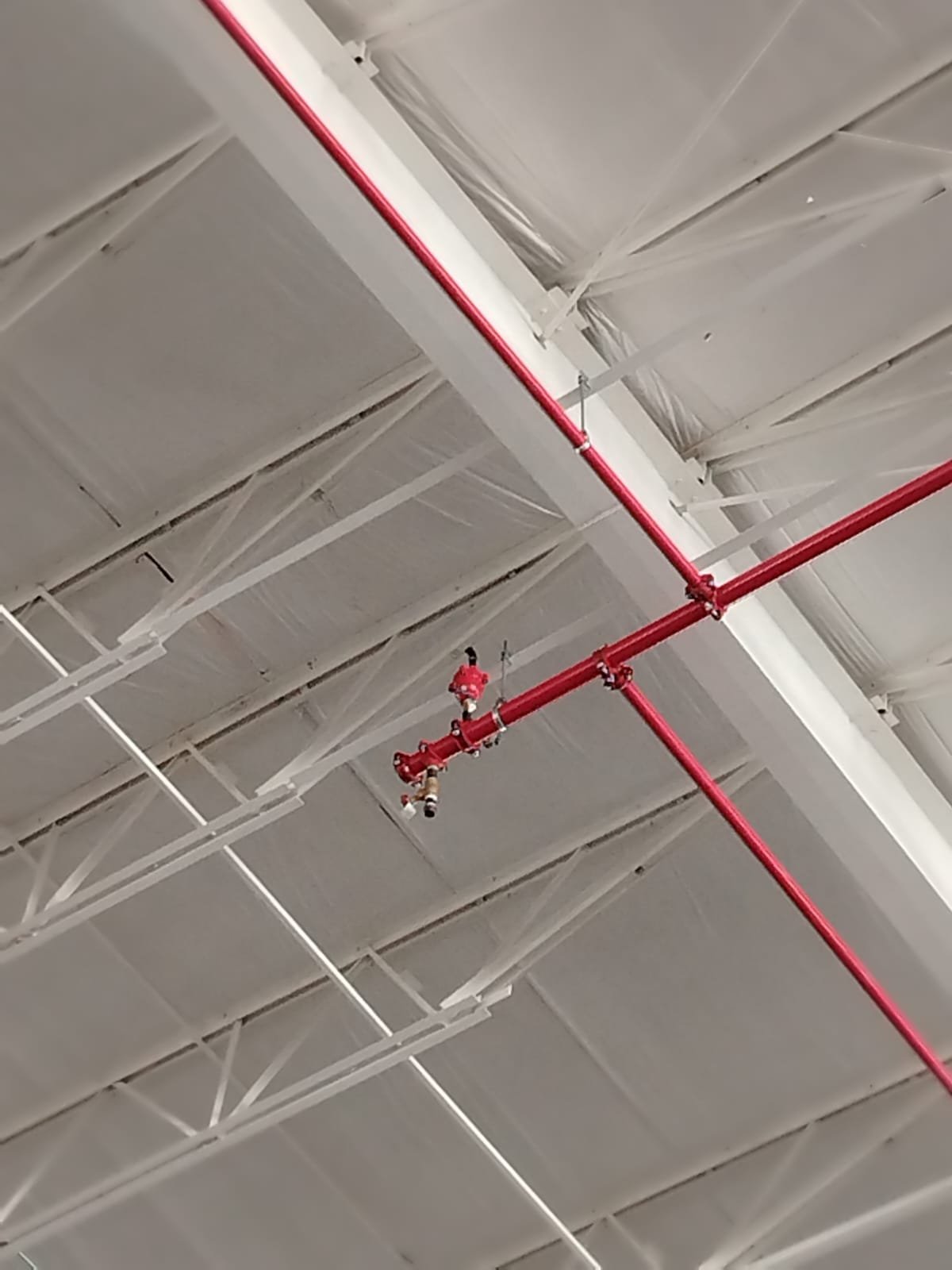 Tubería roja y componentes del sistema contra incendio instalados bajo la cubierta de una nave.